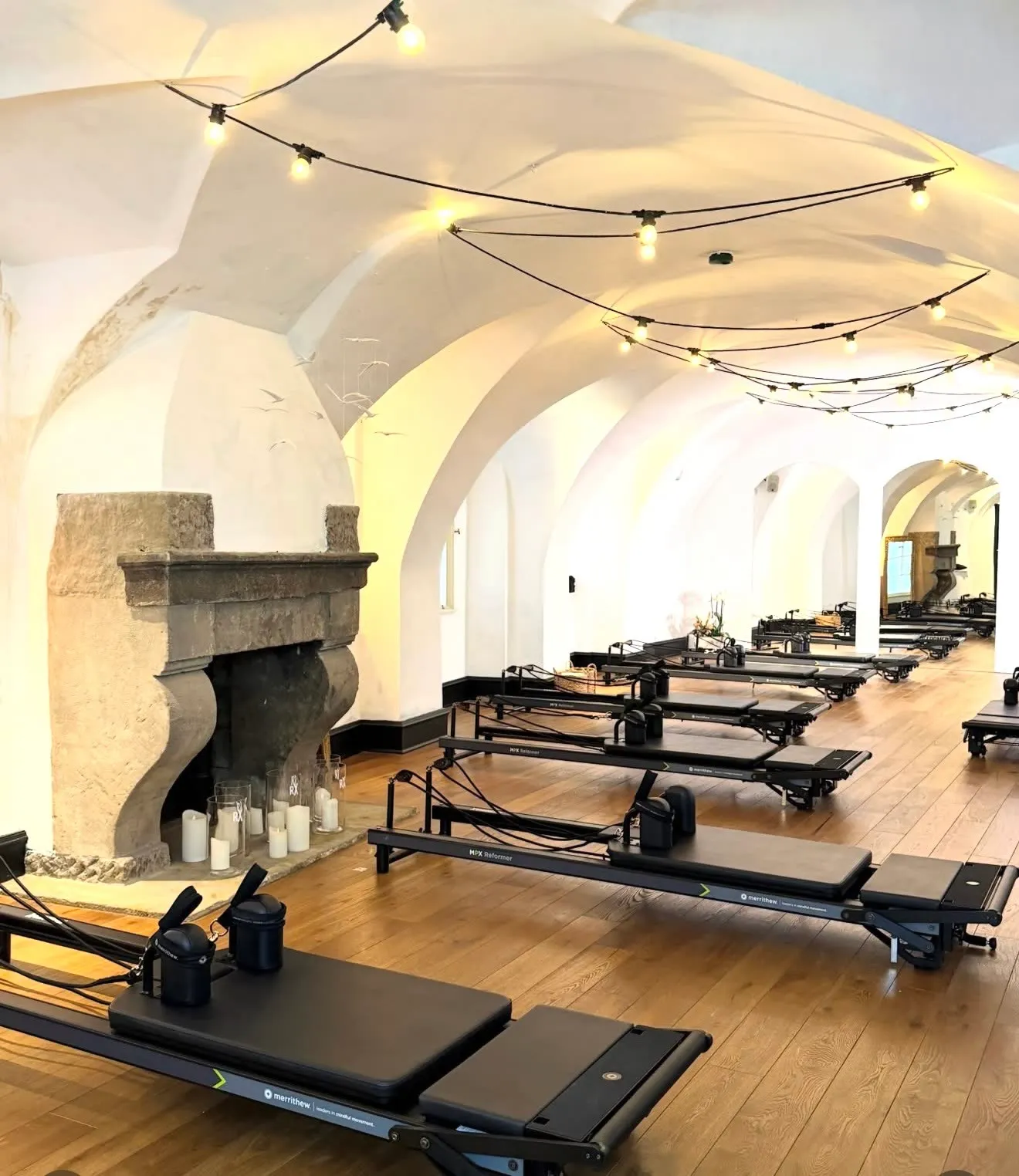 The ReformerX studio hall with vaulted ceilings, a stone fireplace with candles and a row of black reformers